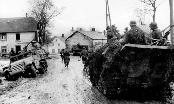 Waffen SS panzergrenadiers move past wrecked American equipment during the 1st days of the Ardennes offensive.