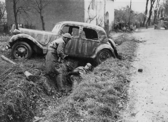 Soldiers of the 2nd Battalion de Choc, French Commandos, take cover behind a shattered German staff car during a firefight in Belfort, France on November 20, 1944.
